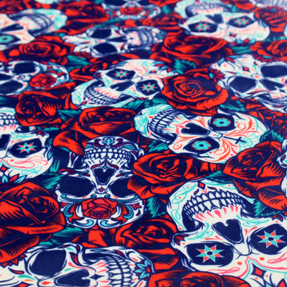 A vibrant repeating pattern on a dark background featuring decorated sugar skulls with intricate blue and red designs, surrounded by deep red roses and green leaves.