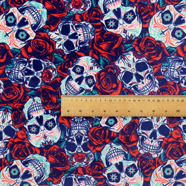 A vibrant repeating pattern on a dark background featuring decorated sugar skulls with intricate blue and red designs, surrounded by deep red roses and green leaves.