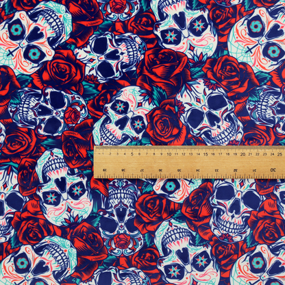 A vibrant repeating pattern on a dark background featuring decorated sugar skulls with intricate blue and red designs, surrounded by deep red roses and green leaves.