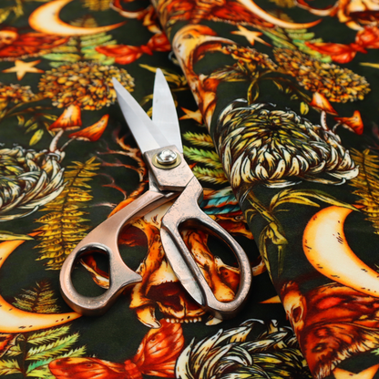 A dark and mystical repeating pattern featuring animal skulls, crescent moons, stars, moths, ferns, and chrysanthemums in warm golden and orange tones.