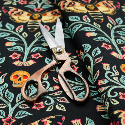 A symmetrical, damask-style repeating pattern on a black background featuring death's-head hawkmoths, human skulls, and ornate scrolling blue-green vines with pink and red flowers.