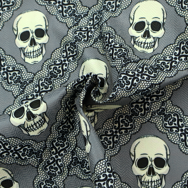 A repeating pattern on a grey background featuring off-white human skulls arranged in a grid, separated by diagonal intersecting bands of ornate black lace with intricate scrollwork.