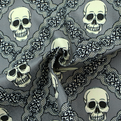 A repeating pattern on a grey background featuring off-white human skulls arranged in a grid, separated by diagonal intersecting bands of ornate black lace with intricate scrollwork.