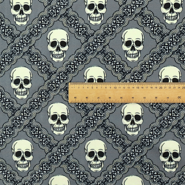A repeating pattern on a grey background featuring off-white human skulls arranged in a grid, separated by diagonal intersecting bands of ornate black lace with intricate scrollwork.