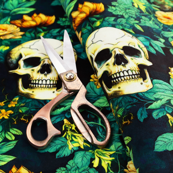A detailed repeating pattern on a dark background featuring ivory human skulls entwined with vibrant green leafy vines and blooming yellow and orange flowers.