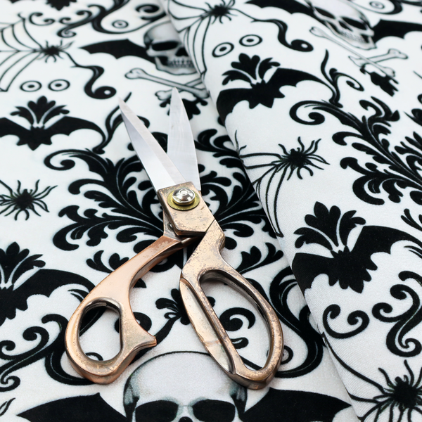 A spooky, ornate damask-style repeating pattern on a white background featuring black skulls, bats, spiderwebs with small spiders, and crossbones.