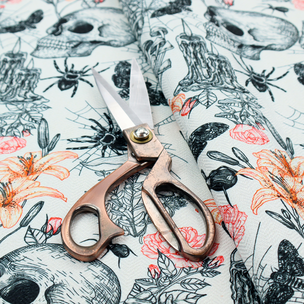 A hand-drawn, sketch-style pattern on an off-white background featuring human skulls, melting candles, spiders, moths, mushrooms, and floral elements like lilies and roses.