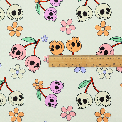 A light retro-style pattern featuring whimsical cherry pairs where the fruit is shaped like colourful skulls in shades of cream, pink, orange, and purple, accented by simple pastel flowers.