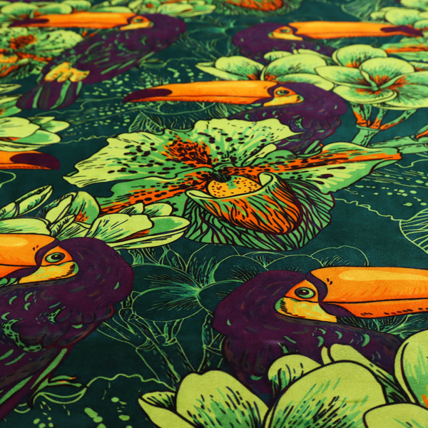A dark green fabric densely patterned with toucans featuring large orange-and-yellow beaks, surrounded by glowing light green and orange tropical flowers.   