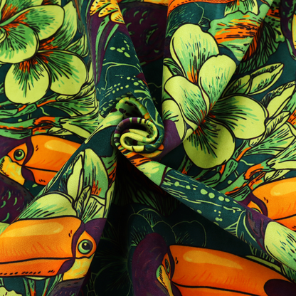 A dark green fabric densely patterned with toucans featuring large orange-and-yellow beaks, surrounded by glowing light green and orange tropical flowers.   