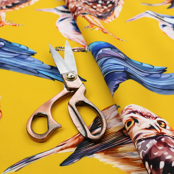 A vibrant yellow fabric patterned with a repeat design of various illustrated birds, including owls, robins, woodpeckers, and bluebirds
