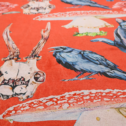 A red fabric patterned with hand-drawn gothic illustrations of black cats, crows, animal skulls, mushrooms, and roses featuring an organic style.