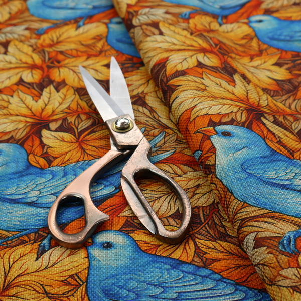 An orange and brown fabric patterned with hand-drawn botanical illustrations of blue birds perched amongst fall leaves featuring an organic style.   
