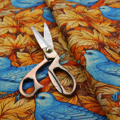 An orange and brown fabric patterned with hand-drawn botanical illustrations of blue birds perched amongst fall leaves featuring an organic style.   
