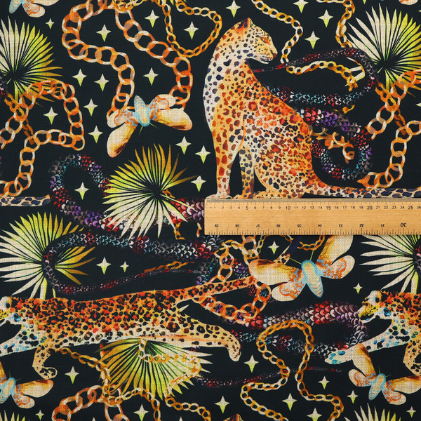A dark blue fabric patterned with hand-drawn jungle illustrations of leopards, golden chains, tropical leaves, and butterflies featuring an organic style.   