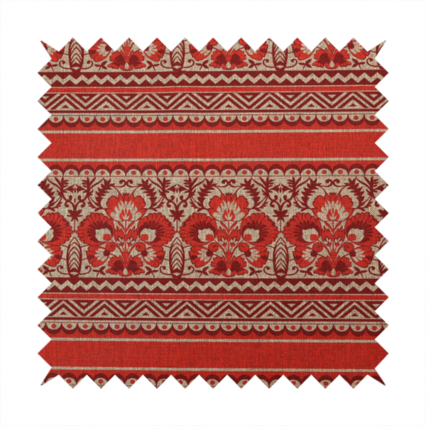 A fabric featuring a folkloric red and beige pattern with horizontal bands of floral motifs, chevrons, and dotted borders.