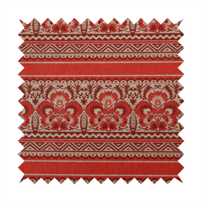 A fabric featuring a folkloric red and beige pattern with horizontal bands of floral motifs, chevrons, and dotted borders.