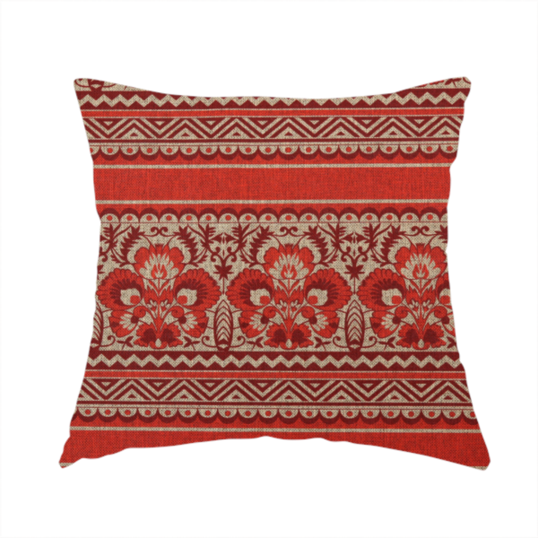 The fabric used to create this handmade cushion is fabric featuring a folkloric red and beige pattern with horizontal bands of floral motifs, chevrons, and dotted borders.