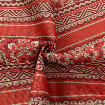 A fabric featuring a folkloric red and beige pattern with horizontal bands of floral motifs, chevrons, and dotted borders.