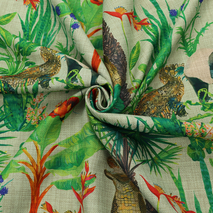 A green and beige fabric patterned with hand-drawn jungle illustrations of alligators, a tapir, tropical trees, and vibrant flowers featuring an organic style.