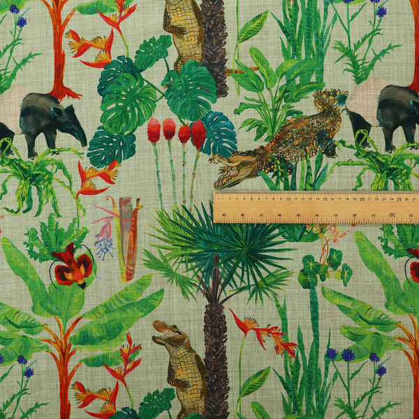 A green and beige fabric patterned with hand-drawn jungle illustrations of alligators, a tapir, tropical trees, and vibrant flowers featuring an organic style.