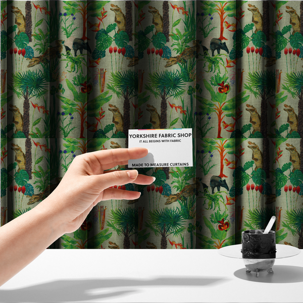 The fabric used to create these made-to-measure curtains is a green and beige fabric patterned with hand-drawn jungle illustrations of alligators, a tapir, tropical trees, and vibrant flowers featuring an organic style.