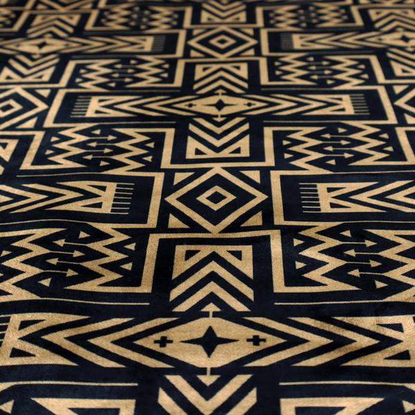 Black and gold geometric fabric featuring an intricate Navajo-inspired tribal pattern with chevron lines, diamonds, and cross motifs.