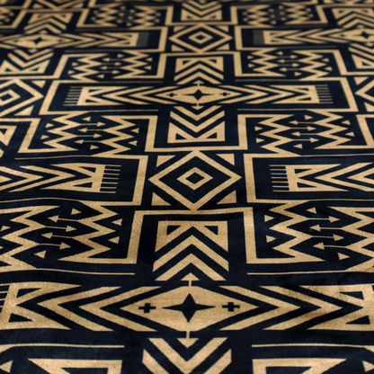Black and gold geometric fabric featuring an intricate Navajo-inspired tribal pattern with chevron lines, diamonds, and cross motifs.