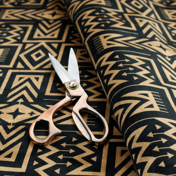 Black and gold geometric fabric featuring an intricate Navajo-inspired tribal pattern with chevron lines, diamonds, and cross motifs.
