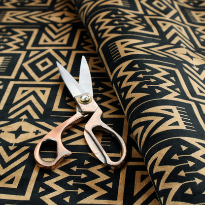 Black and gold geometric fabric featuring an intricate Navajo-inspired tribal pattern with chevron lines, diamonds, and cross motifs.