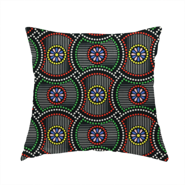 The fabric used to create this handmade cushion is a vibrant multi-coloured fabric featuring a detailed dotted pattern with concentric circular motifs, floral-like centre rosettes, and striped geometric panels in black, red, green, blue, and yellow.   