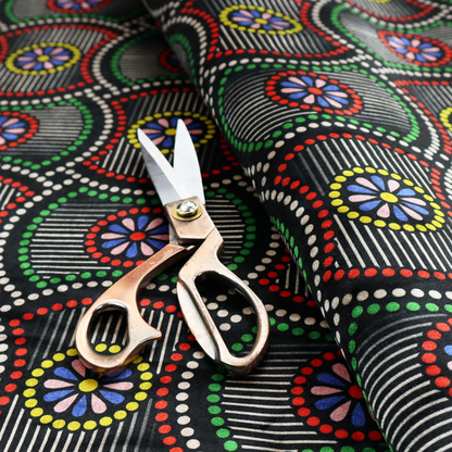 Vibrant multi-coloured fabric featuring a detailed dotted pattern with concentric circular motifs, floral-like centre rosettes, and striped geometric panels in black, red, green, blue, and yellow.   