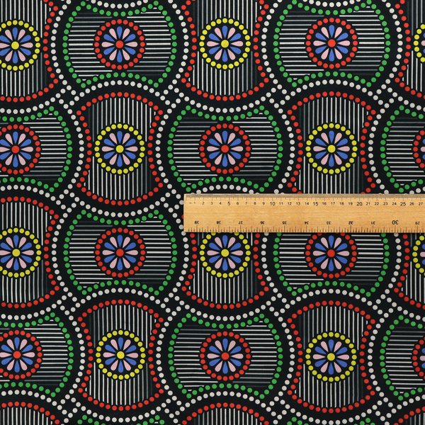 Vibrant multi-coloured fabric featuring a detailed dotted pattern with concentric circular motifs, floral-like centre rosettes, and striped geometric panels in black, red, green, blue, and yellow.   