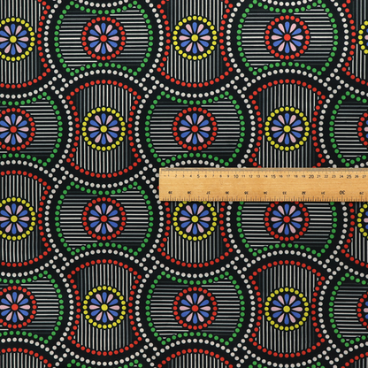 Vibrant multi-coloured fabric featuring a detailed dotted pattern with concentric circular motifs, floral-like centre rosettes, and striped geometric panels in black, red, green, blue, and yellow.   