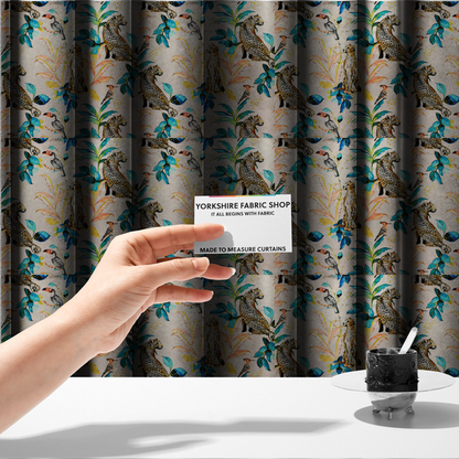The fabric used to create these made-to-measure curtains is an exotic cream, blue, and orange fabric featuring a tropical jungle pattern with leopards, cheetahs, toucans, exotic birds, and lush foliage.   