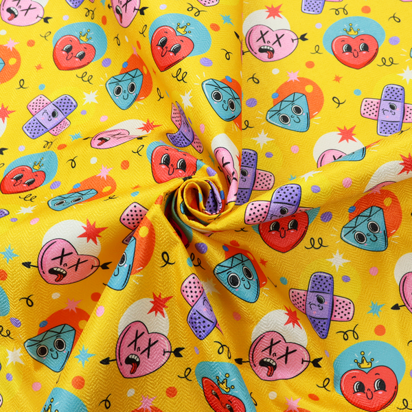 Yellow fabric featuring a playful, quirky pattern with cartoon-style graphics including smiling hearts with crowns, cute diamonds, cartoon bandages, and wacky faces with X eyes on a bright yellow background.   