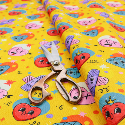 Yellow fabric featuring a playful, quirky pattern with cartoon-style graphics including smiling hearts with crowns, cute diamonds, cartoon bandages, and wacky faces with X eyes on a bright yellow background.   