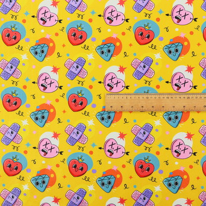 Yellow fabric featuring a playful, quirky pattern with cartoon-style graphics including smiling hearts with crowns, cute diamonds, cartoon bandages, and wacky faces with X eyes on a bright yellow background.   