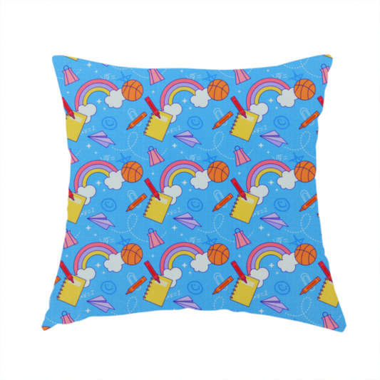 The fabric used to create this handmade cushion is a blue fabric featuring a playful back-to-school pattern with colourful rainbows, basketballs, yellow notebooks with red pencils, purple paper airplanes, and school supplies scattered across a bright blue background.