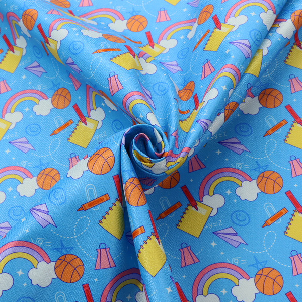 Blue fabric featuring a playful back-to-school pattern with colourful rainbows, basketballs, yellow notebooks with red pencils, purple paper airplanes, and school supplies scattered across a bright blue background.