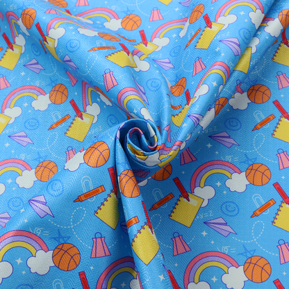 Blue fabric featuring a playful back-to-school pattern with colourful rainbows, basketballs, yellow notebooks with red pencils, purple paper airplanes, and school supplies scattered across a bright blue background.