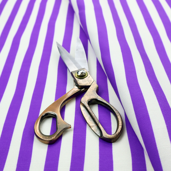 A white fabric patterned with vertical, hand-drawn purple stripes that feature a slight, organic waviness.
