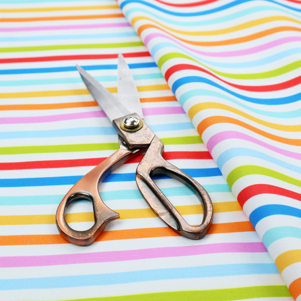 A white fabric patterned with horizontal, hand-drawn multi-coloured stripes in pink, blue, green, red, yellow, and orange that feature a slight, organic waviness.   