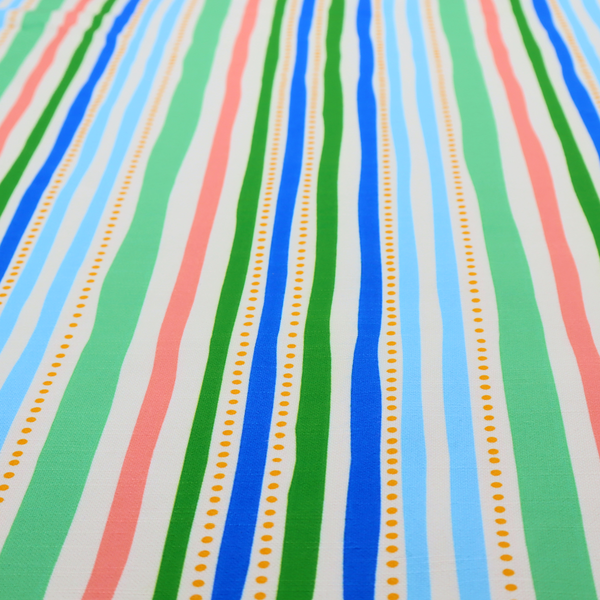 A white fabric patterned with vertical, hand-drawn multi-coloured stripes in green, blue, pink, and light blue alongside dotted lines that feature an organic waviness.
