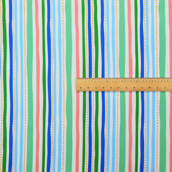 A white fabric patterned with vertical, hand-drawn multi-coloured stripes in green, blue, pink, and light blue alongside dotted lines that feature an organic waviness.