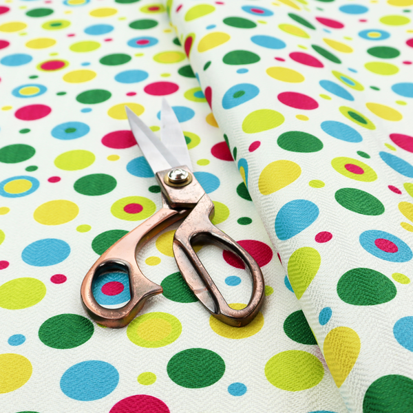 A playful fabric pattern featuring scattered polka dots and concentric circles in various sizes and colours, including pink, blue, green, yellow, and lime on a white background.