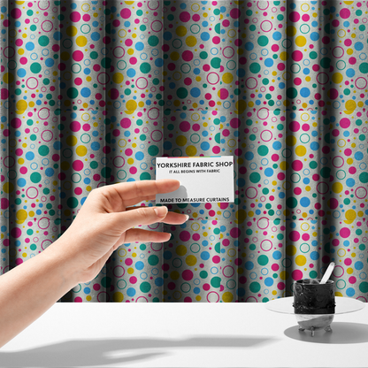 The fabric used to create these made-to-measure curtains is a fun and colourful fabric pattern featuring random solid and hollow polka dots in pink, teal, yellow, and blue on a white background.