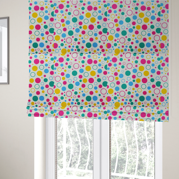 The fabric used to create these Roman blinds is a fun and colourful fabric pattern featuring random solid and hollow polka dots in pink, teal, yellow, and blue on a white background.