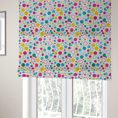 The fabric used to create these Roman blinds is a fun and colourful fabric pattern featuring random solid and hollow polka dots in pink, teal, yellow, and blue on a white background.