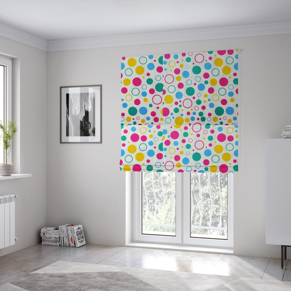 The fabric used to create these Roman blinds is a fun and colourful fabric pattern featuring random solid and hollow polka dots in pink, teal, yellow, and blue on a white background.